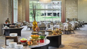 A spacious banquet hall with round tables, a central chandelier, and a view of a golf course through large windows. - Hilton Dallas/Plano Granite Park (Plano)