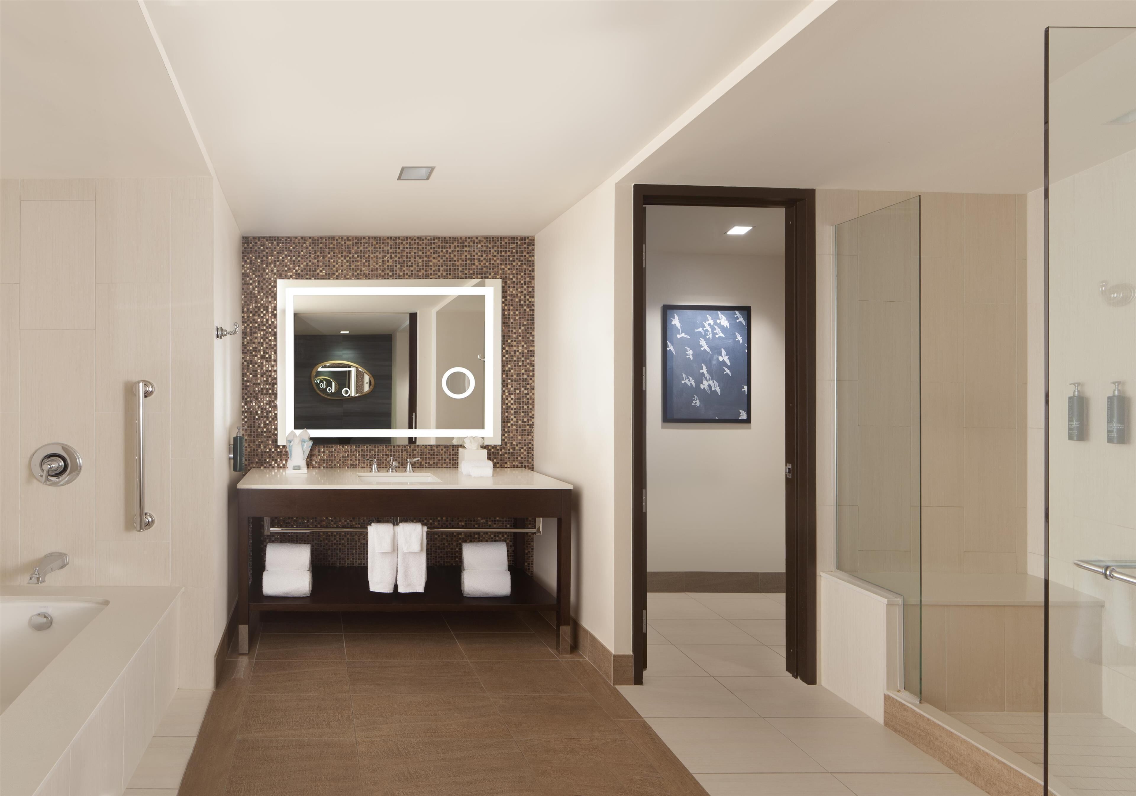 A modern bathroom with a large mirror, a bathtub, a shower area, and a vanity with towels.