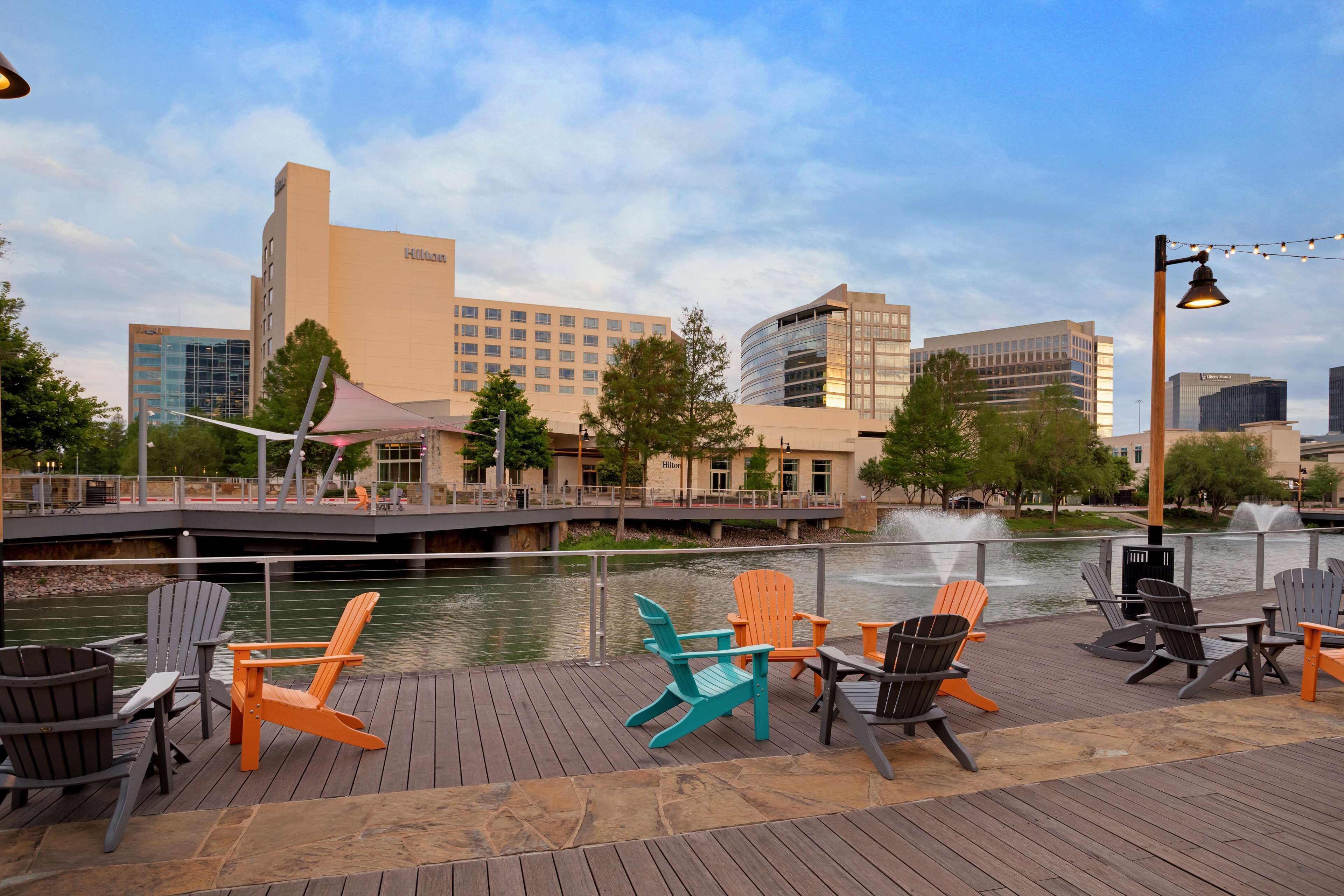 A waterfront deck with Adirondack chairs and a view of the Hilton hotel and other buildings.