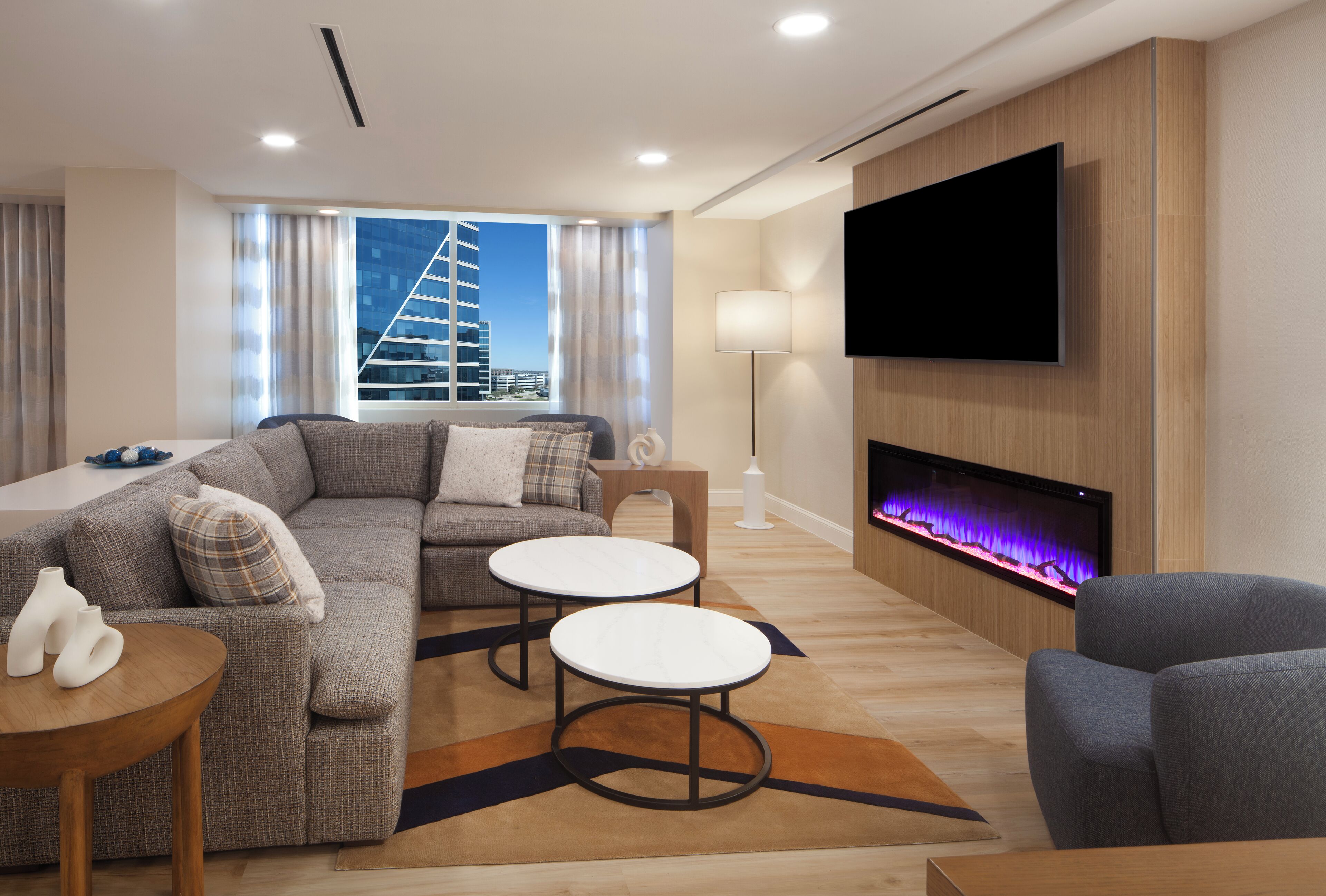 A modern living room with a sofa, two round tables, a flat-screen TV, and a fireplace.