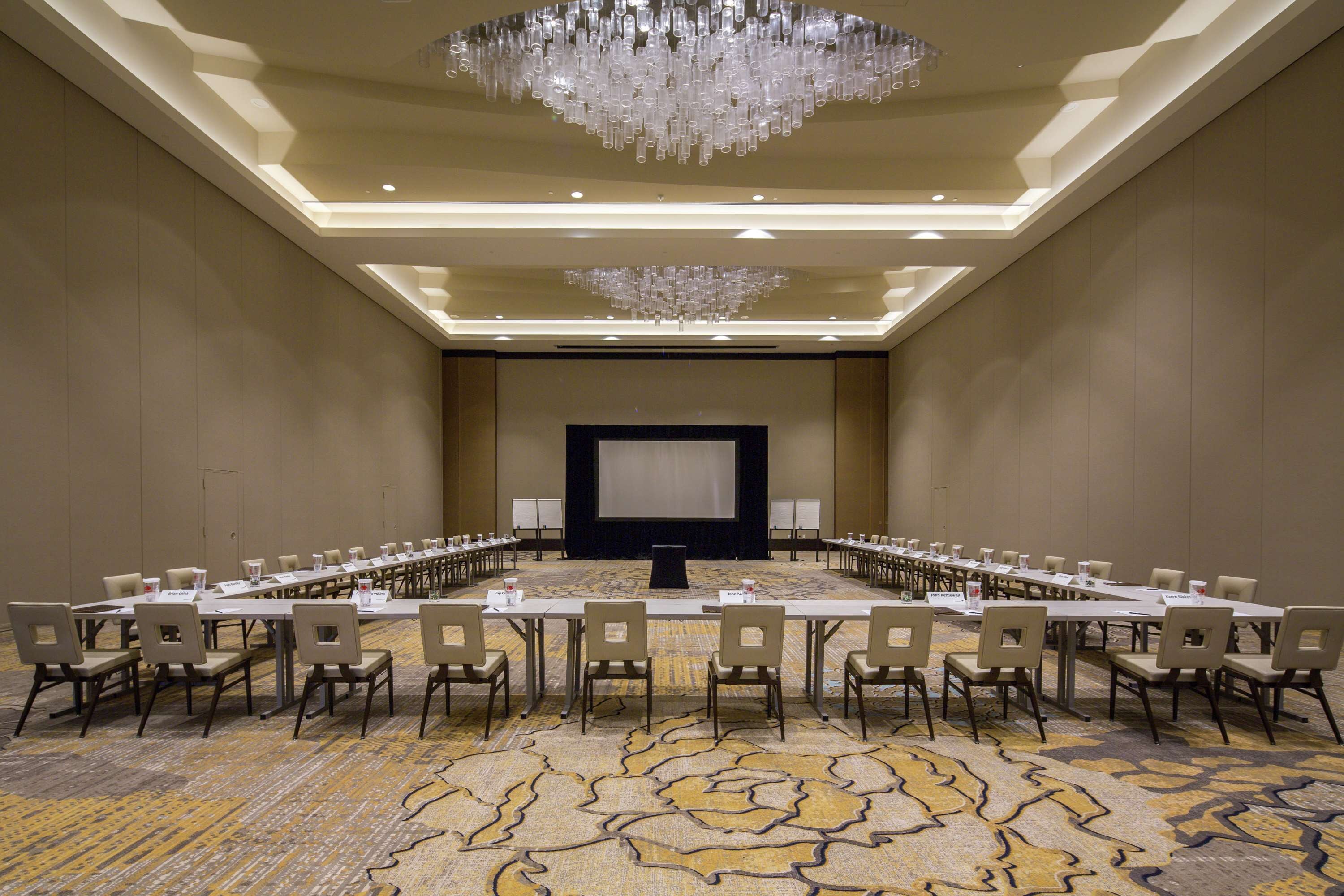 A conference room with a long table, chairs, a projector screen, and a chandelier.