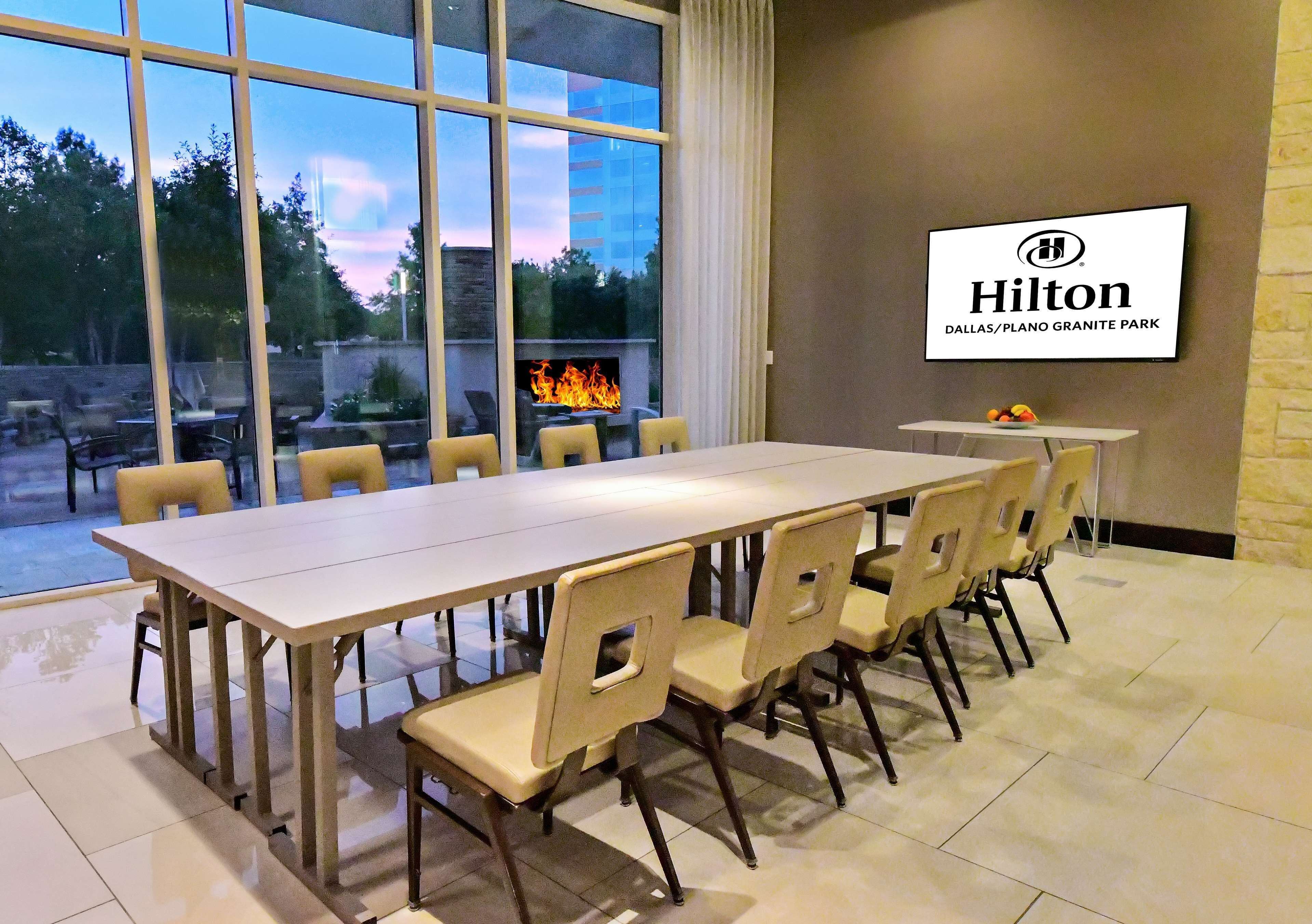 A dining area with a large table and chairs, a fire feature, and a view of the outdoors.