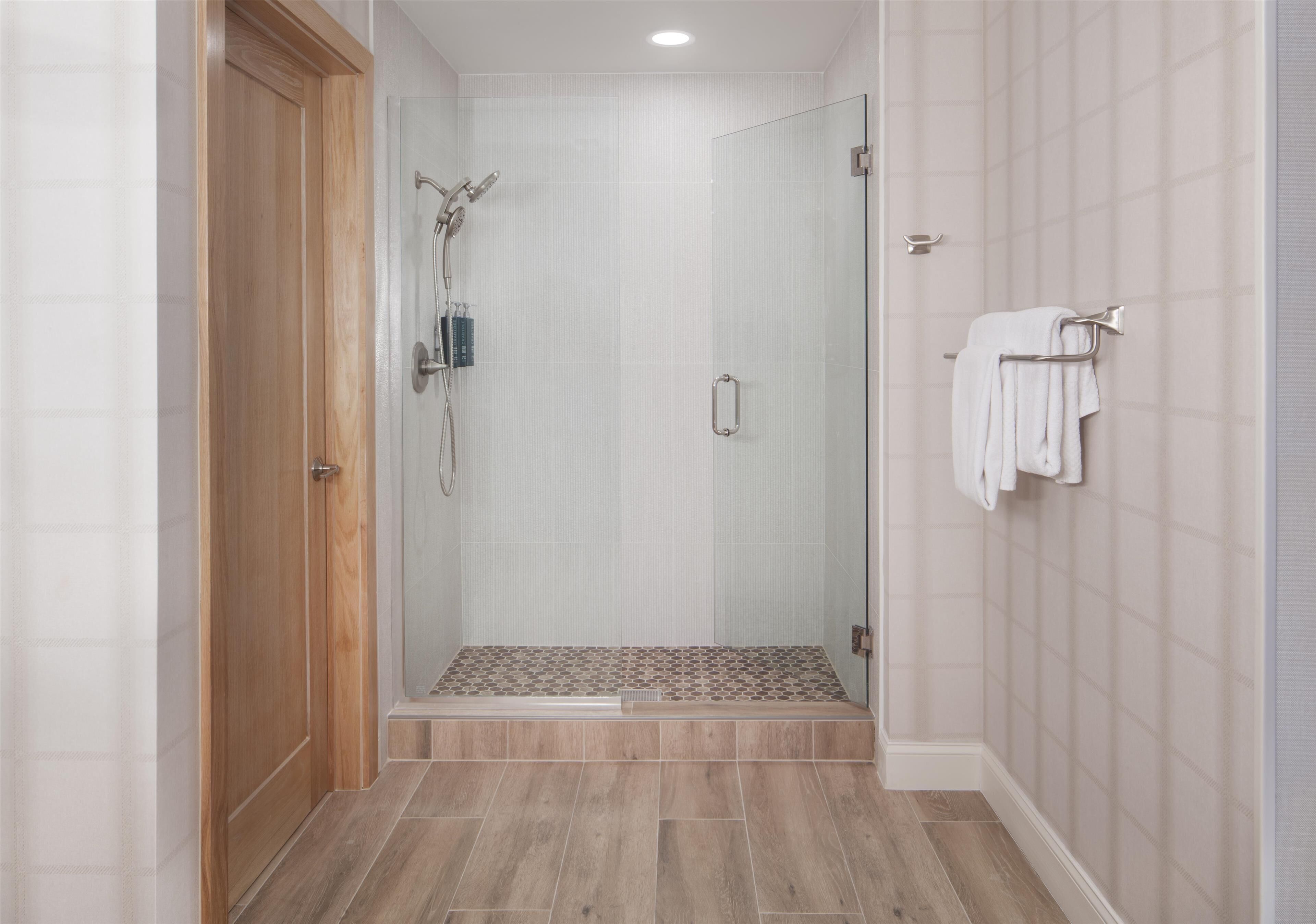 Un baño moderno con cabina de ducha de vidrio, suelo de madera y un perchero para toallas.