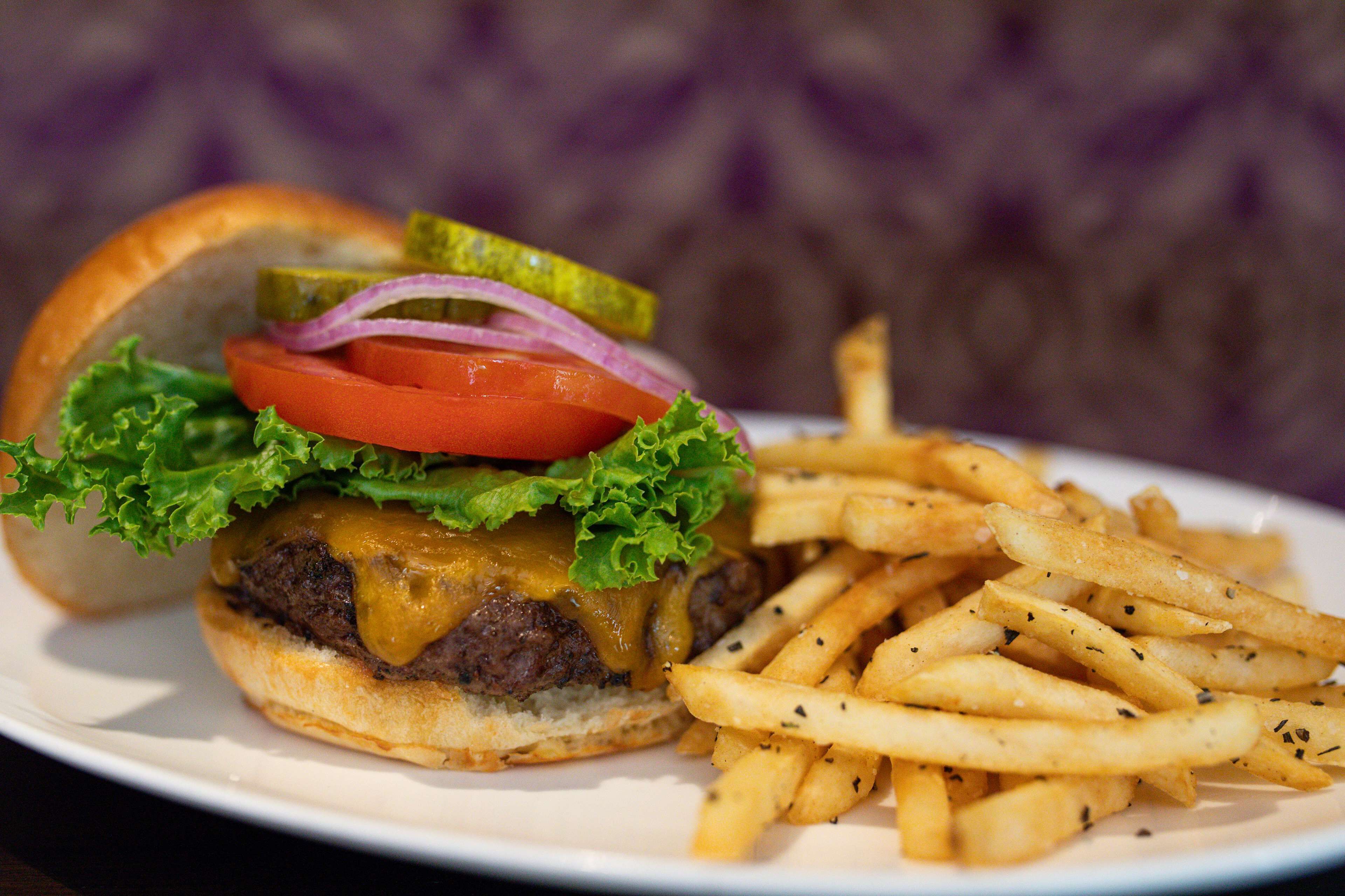Hamburguesa con lechuga, tomate y pepinillo en pan, acompañada de papas fritas sazonadas.