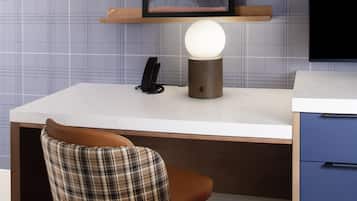Una habitación moderna con un escritorio de mármol blanco, un sillón a cuadros, una obra de arte enmarcada en la pared, una lámpara de mesa redonda y un teléfono.