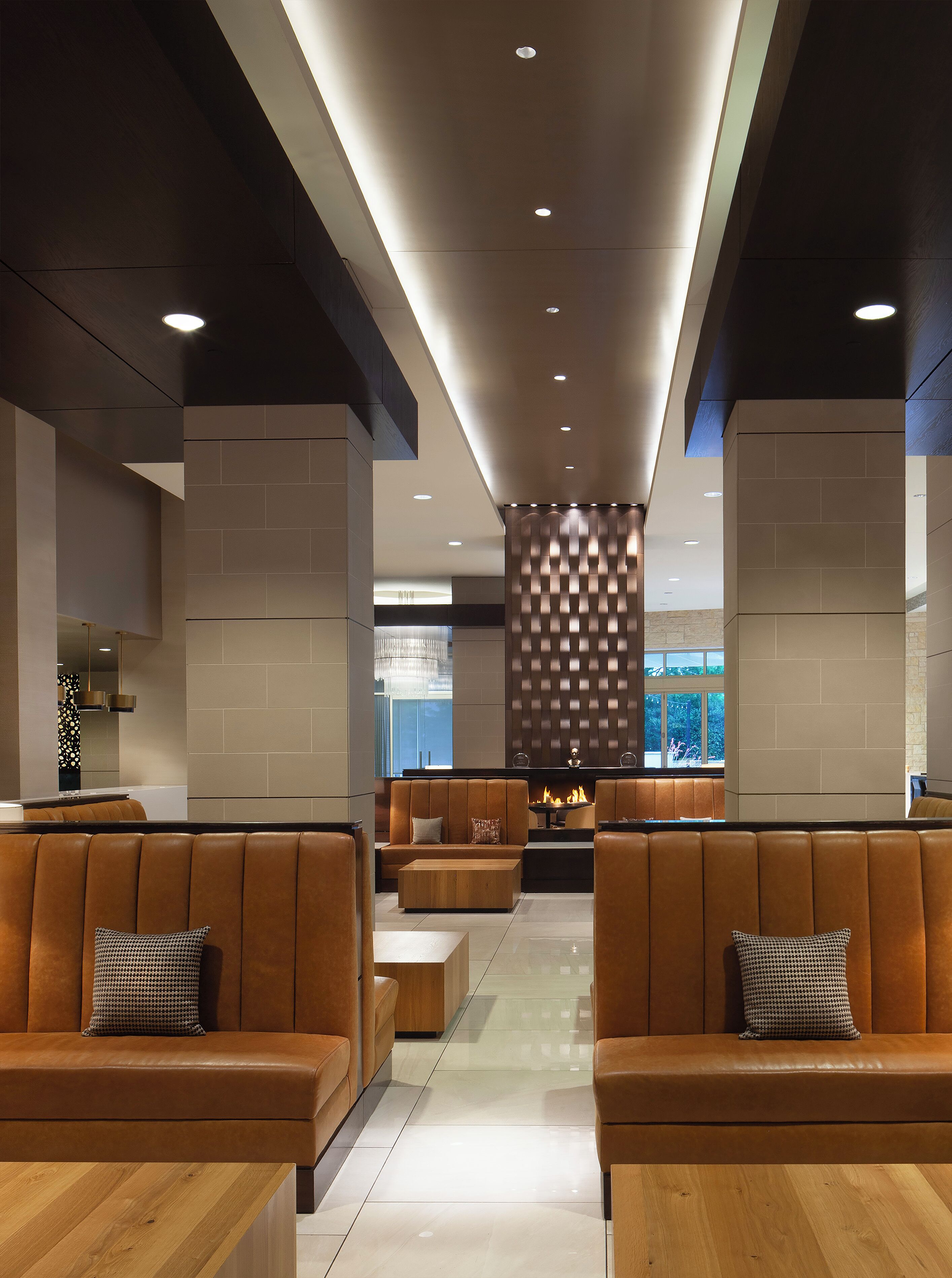 A modern lobby with leather seating, a central fireplace, and a view of the outdoors.