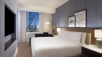 A hotel room with a large bed, a flat-screen TV mounted on the wall, a desk with a lamp, and artwork on the wall.
