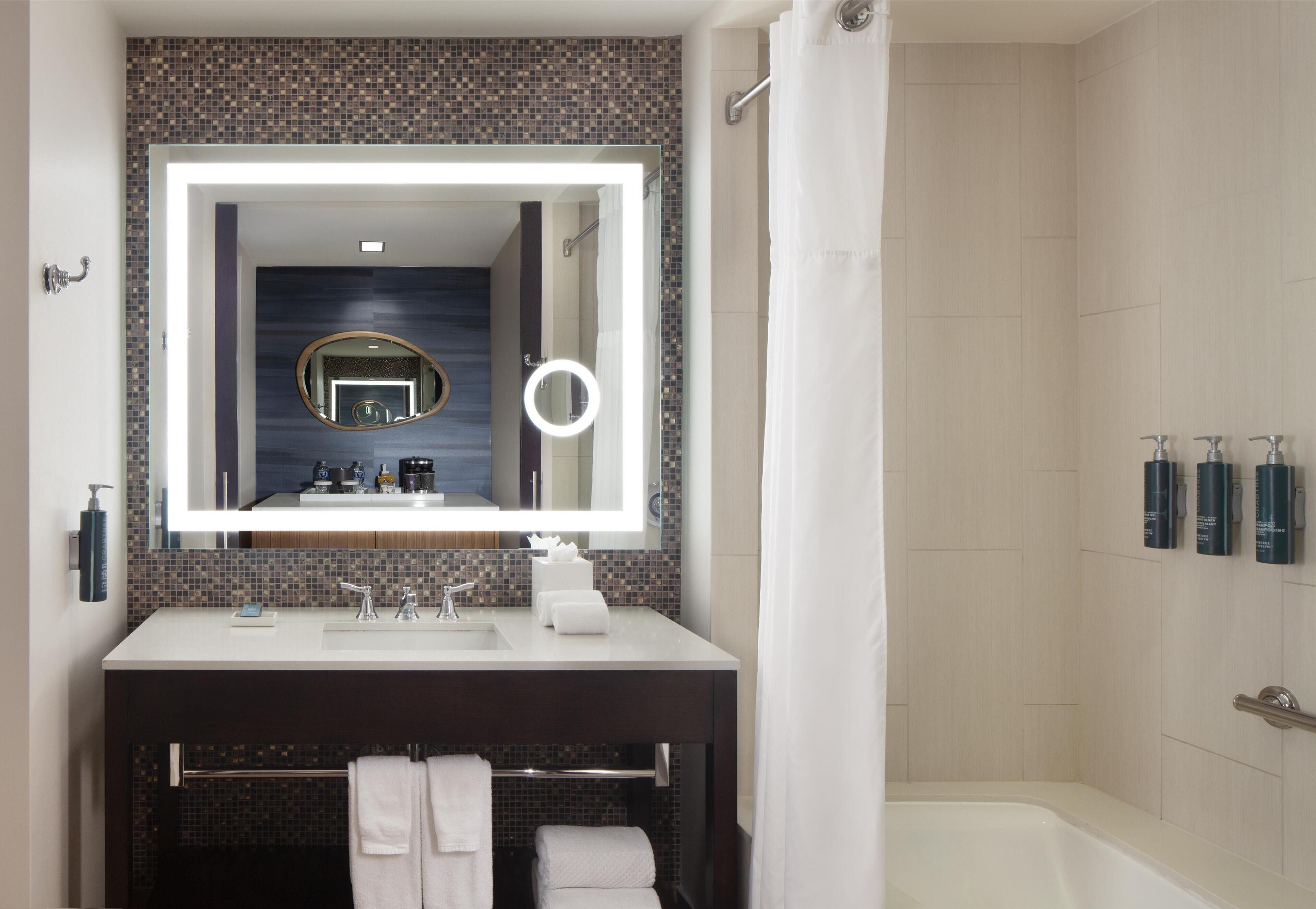 A modern bathroom with a large mirror, a bathtub, and a vanity with a towel rack.