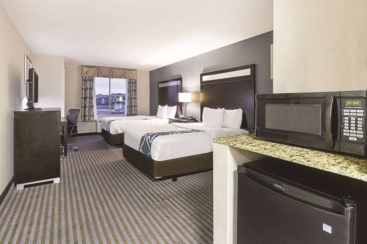 A hotel room with two beds, a desk with a computer, a microwave, and a refrigerator.