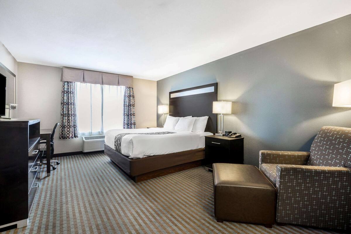 A hotel room with a bed, a desk, a chair, and a small table.