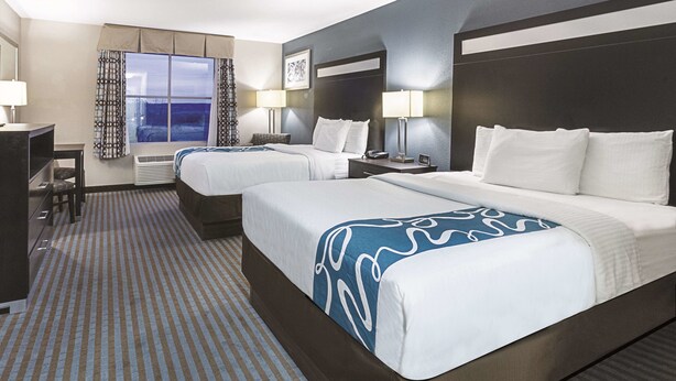 A hotel room with two beds, a desk, and a window with curtains. - La Quinta Inn & Suites by Wyndham Glendive (Glendive)