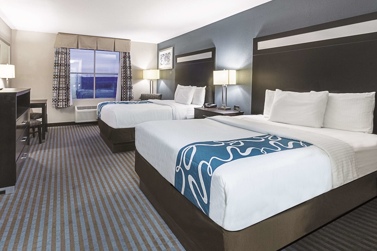 A hotel room with two beds, a desk, and a window with curtains.