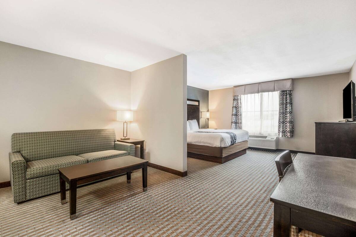 A hotel room with a sofa, a bed, a desk, and a lamp.
