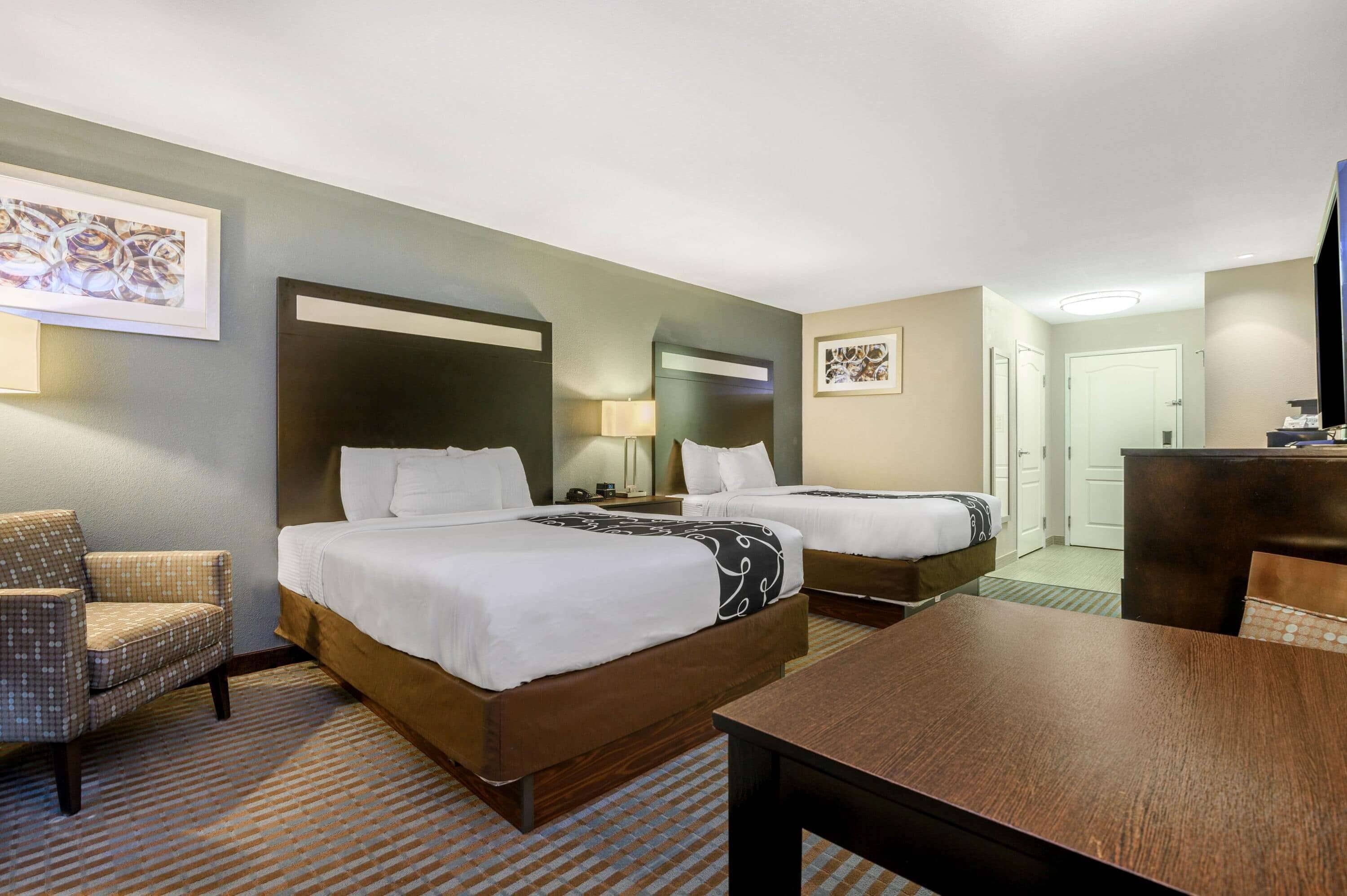 Quarto de hotel com duas camas, uma cadeira, uma mesa e obras de arte nas paredes.