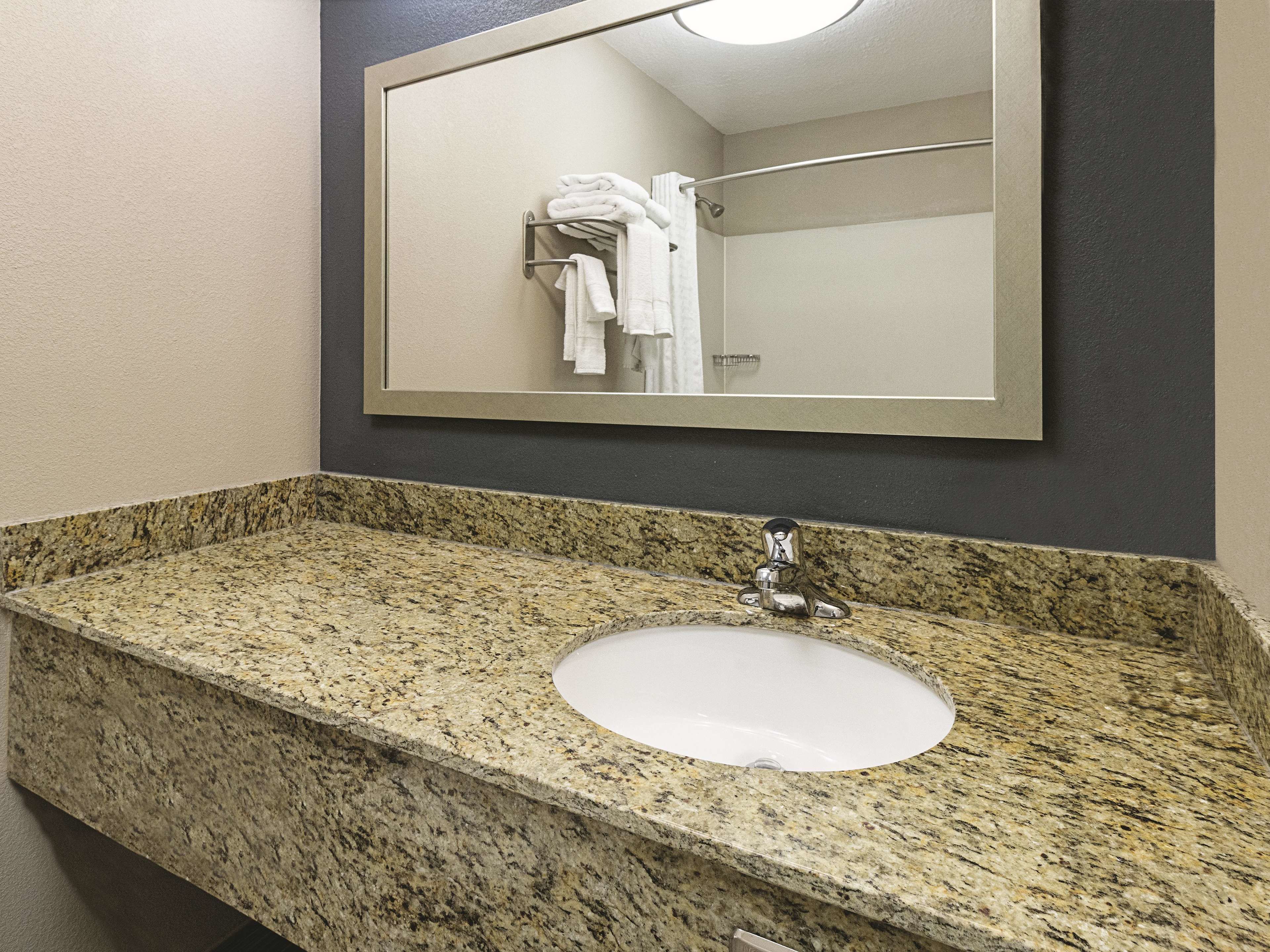 A bathroom with a granite countertop sink, a mirror, and a towel rack with folded towels.