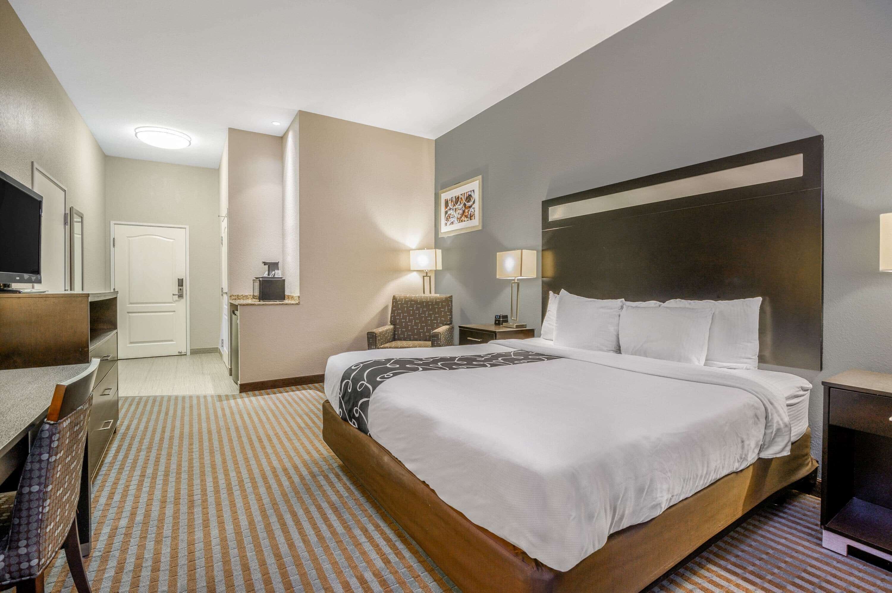 A hotel room with a large bed, a desk with a chair, a television, and a small table with a lamp.