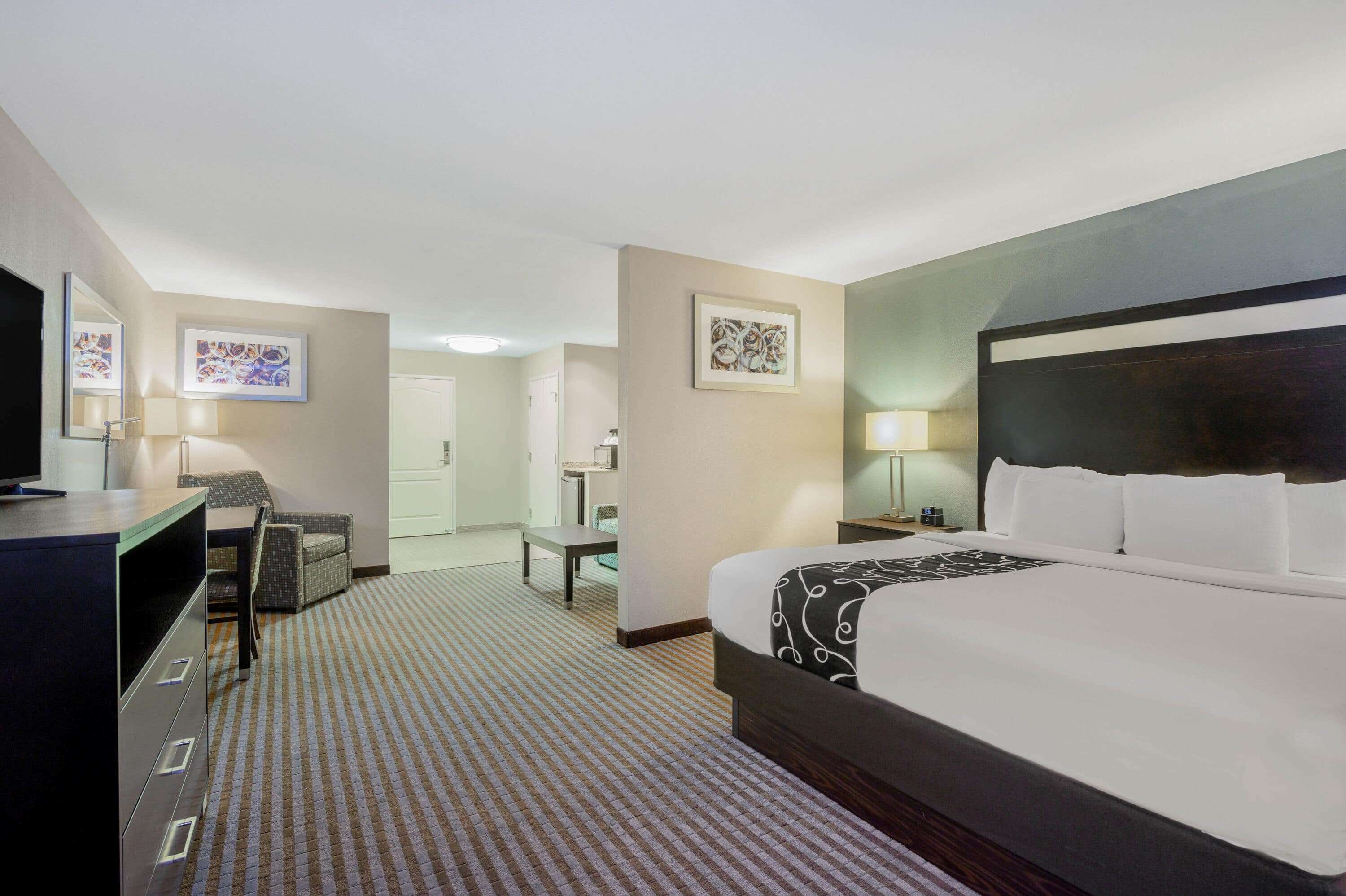 A hotel room with a large bed, a desk, a chair, and a mirror.