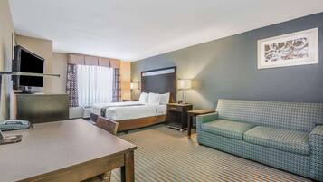 A hotel room with a bed, a sofa, a desk, and a television.