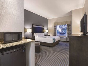 A hotel room with a bed, a desk with a microwave, a TV, and a window with a view of the outside. - La Quinta Inn & Suites by Wyndham Glendive (Glendive)
