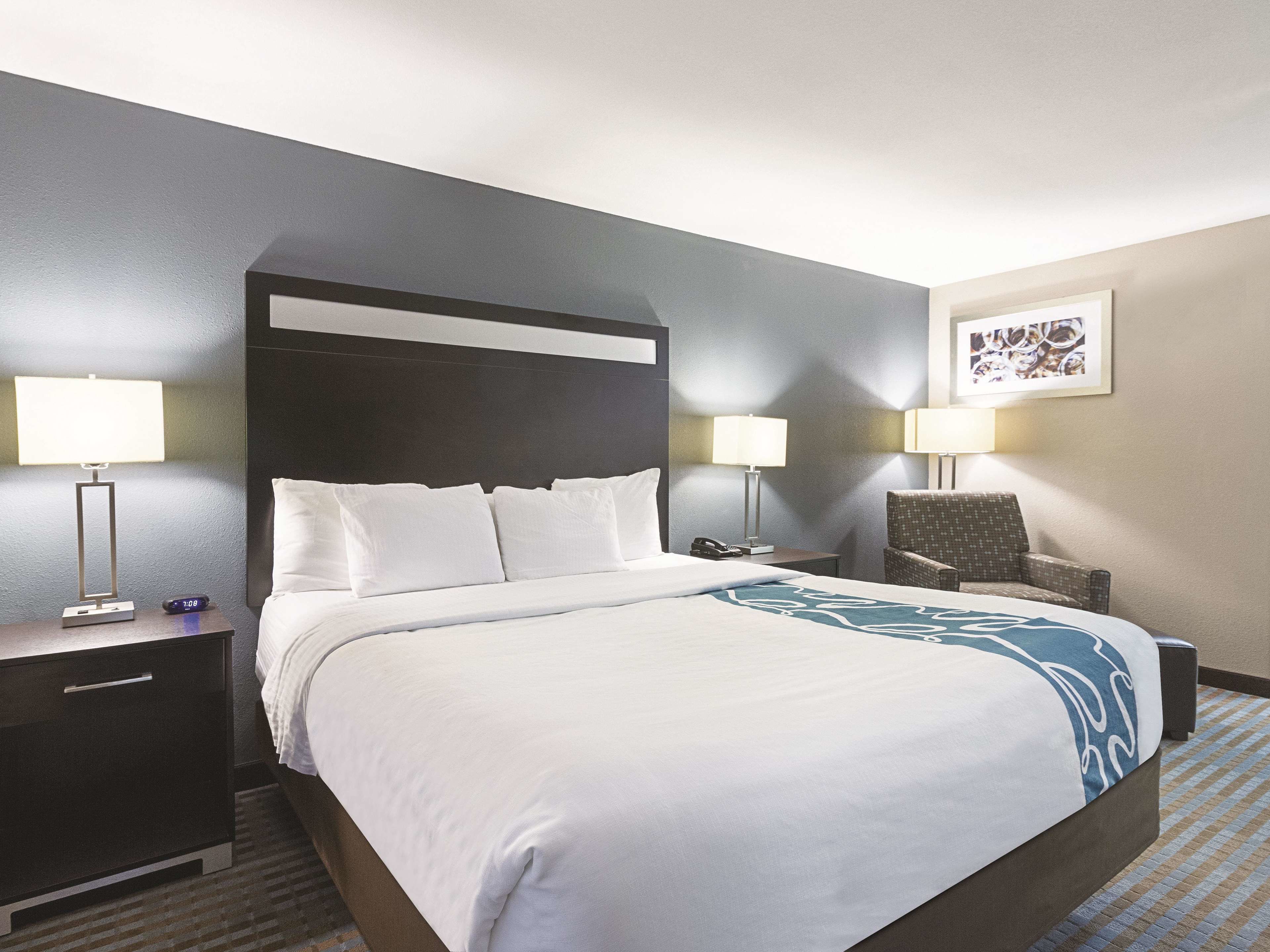 A hotel room with a large bed, two bedside tables, a chair, and a wall-mounted lamp.