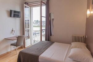 Une chambre à coucher avec un lit, un bureau, une chaise, une télévision et une vue sur l’extérieur.