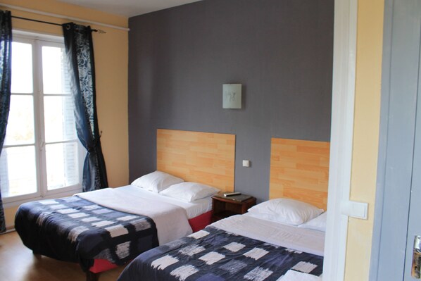 Una habitación de hotel con dos camas, una ventana con cortinas, un cabecero de madera y una mesita de noche pequeña.