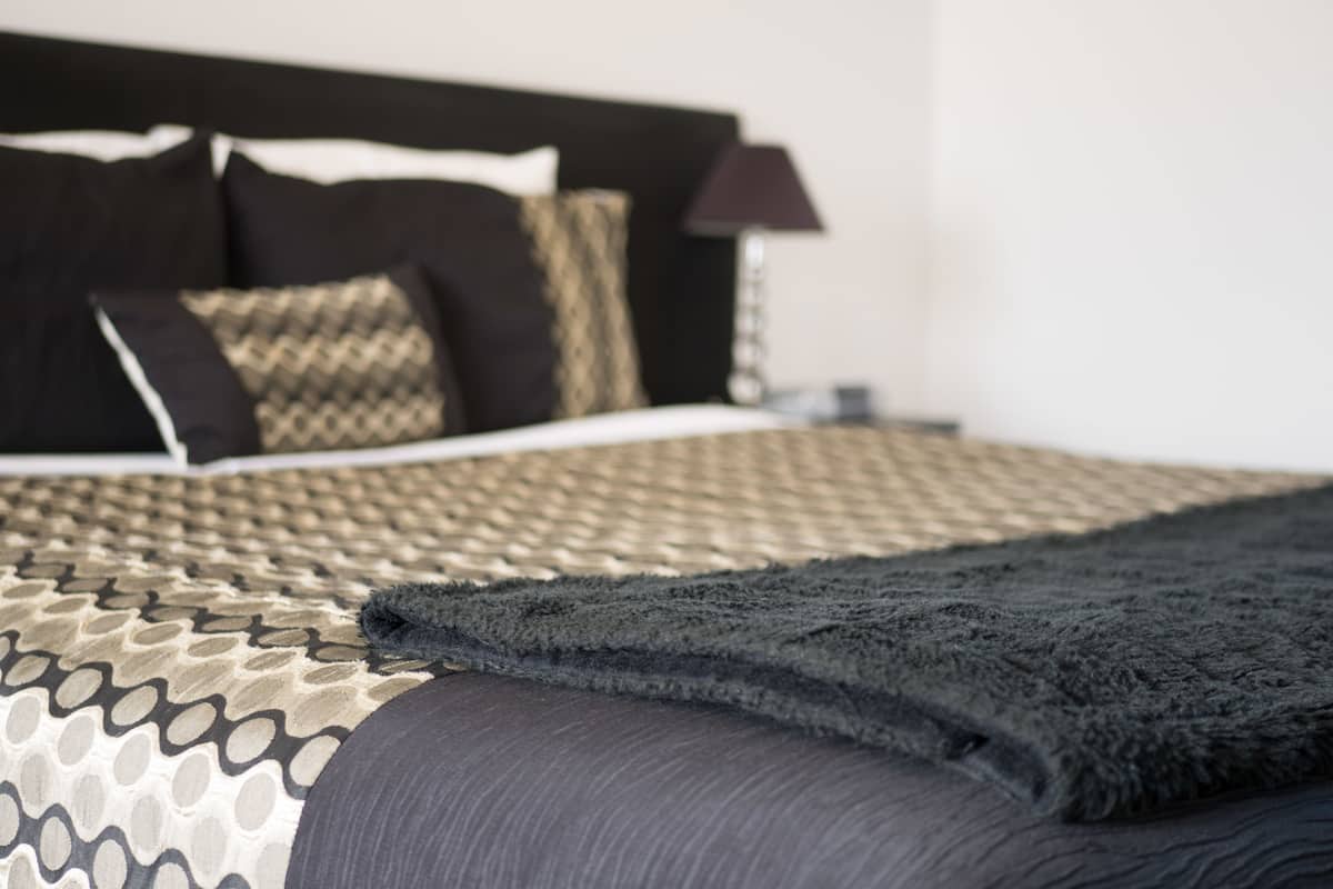 A neatly made bed with a patterned bedspread and a dark throw blanket.