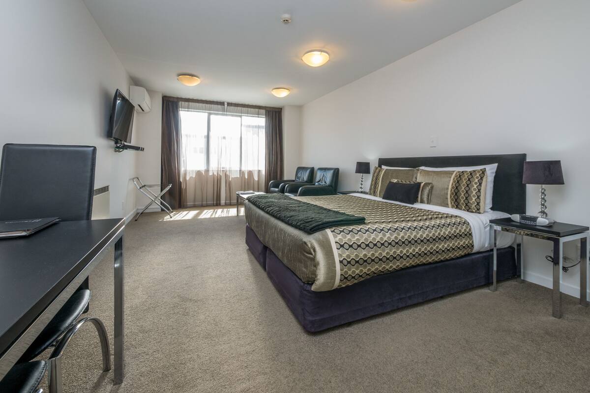 A hotel room with a bed, desk, chair, and a TV mounted on the wall.