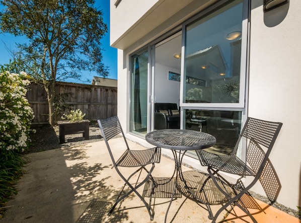 Une terrasse avec une table ronde et quatre chaises, une clôture en bois et un arbre aux fleurs blanches.