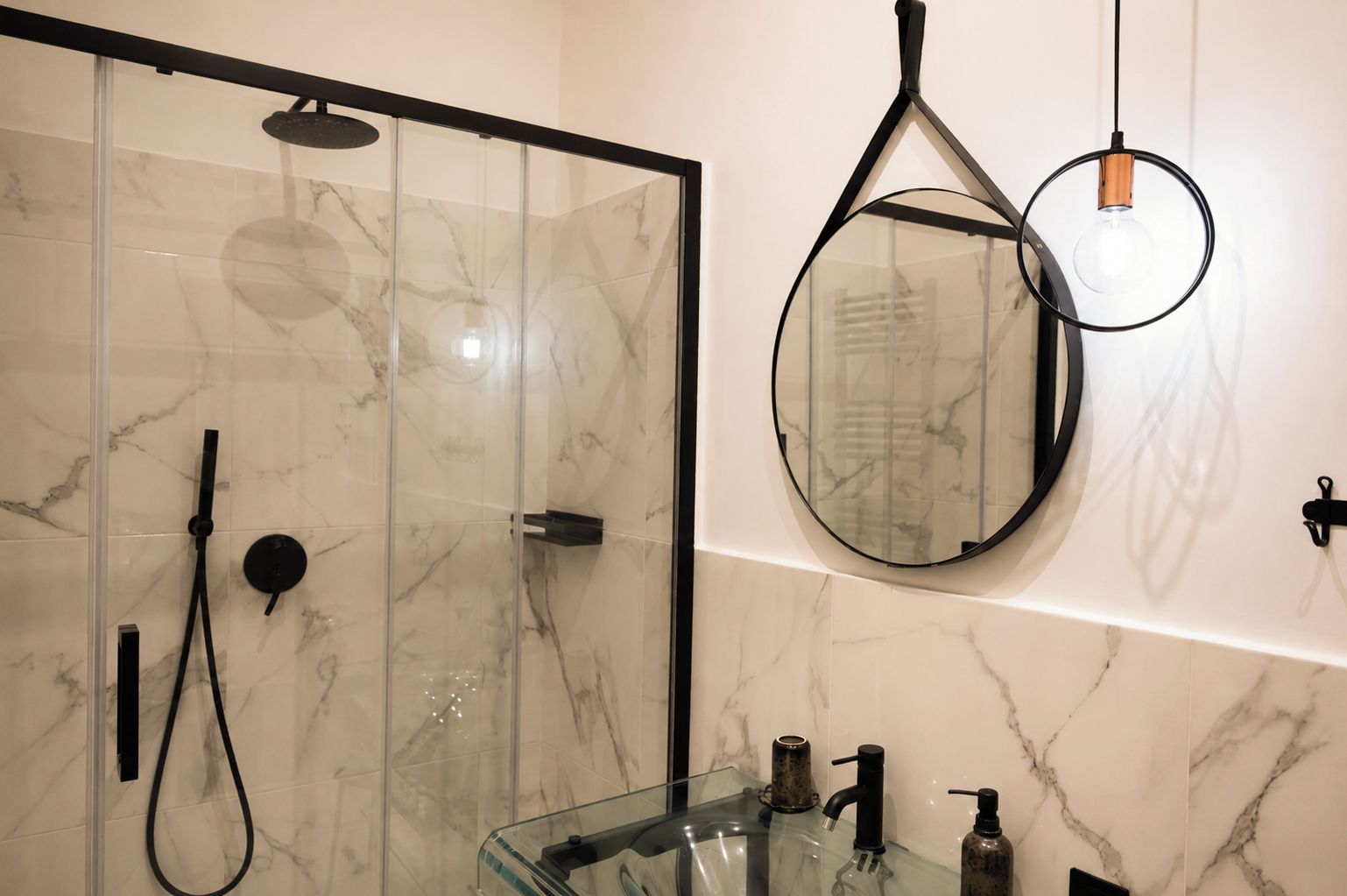 Un baño moderno con cabina de ducha de vidrio, un espejo redondo y un lavabo de vidrio con grifo negro.