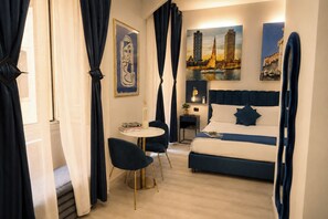 A hotel room with a bed, a round table, and a chair. There are curtains, a painting, and a lamp on the wall. - City Life Rome (Rome)
