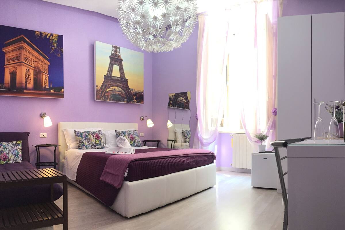 A bedroom with a bed, a desk, a chair, a mirror, and a window with curtains.