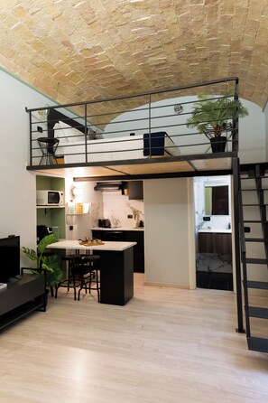 Un espace de vie compact comprenant une chambre en mezzanine, une kitchenette et un coin repas.
