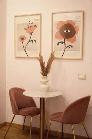A room with two framed artworks, a white vase with dried plants, and two pink chairs with gold legs. - City Life Rome (Rome)