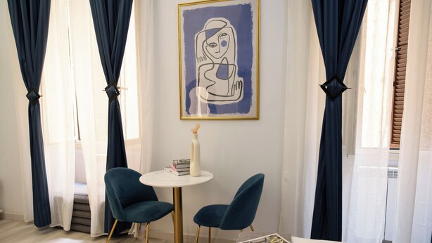 Ein Zimmer mit einem runden Tisch, zwei Stühlen, einem gerahmten Kunstwerk und einer Vase.