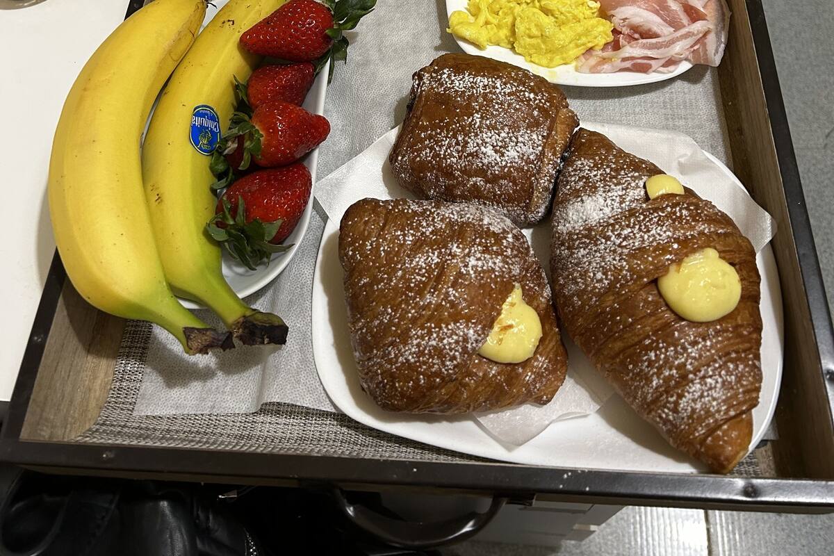 A tray with breakfast items including croissants, strawberries, bananas, scrambled eggs, bacon, and pastries.