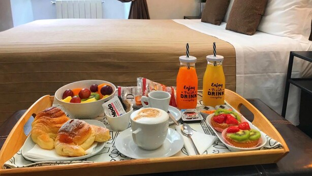 A breakfast tray with croissants, fruit, coffee, and juice on a wooden tray in a hotel room. - City Life Rome (Rome)