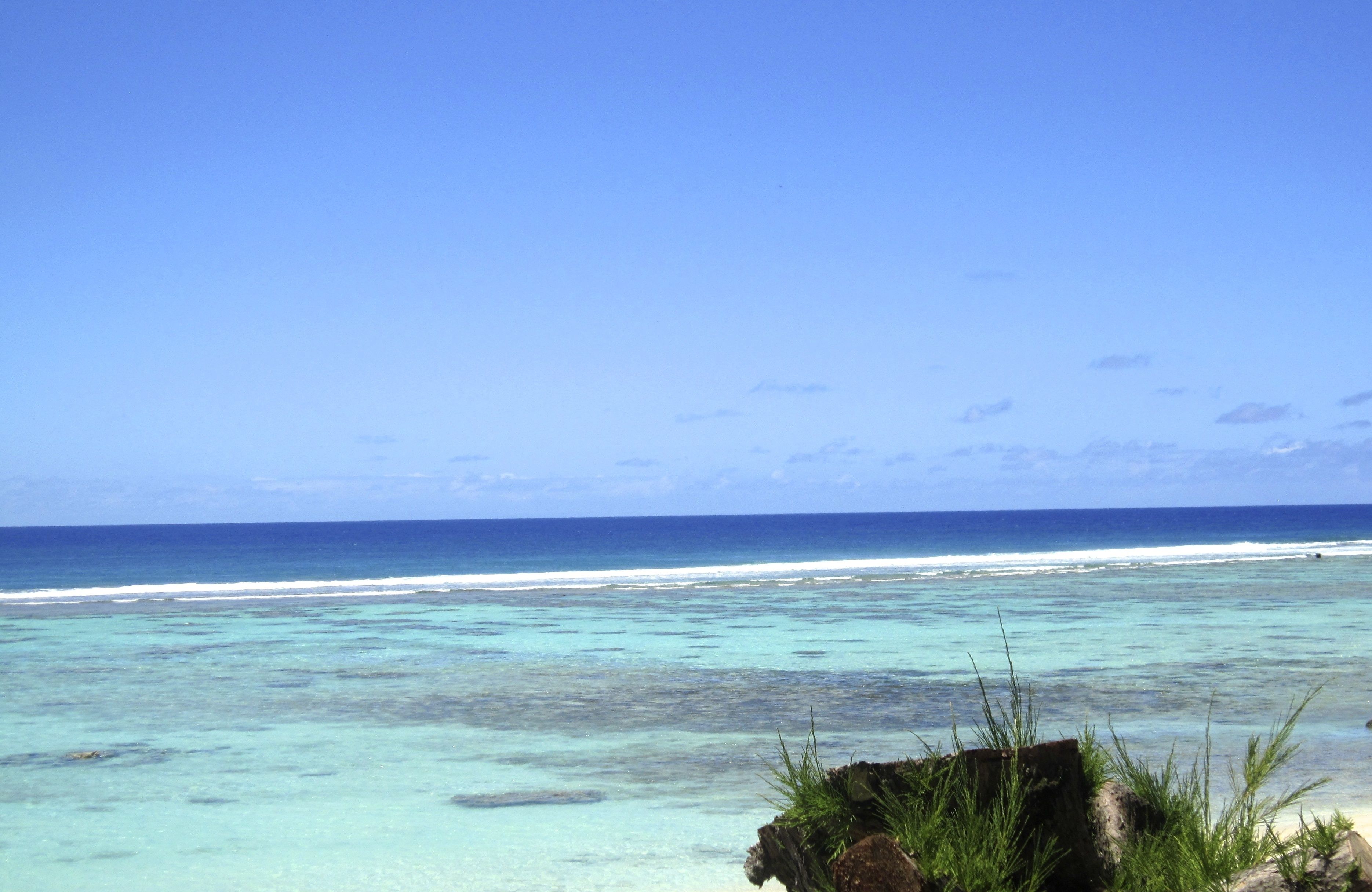 A beach with clear turquoise water and a rocky foreground.