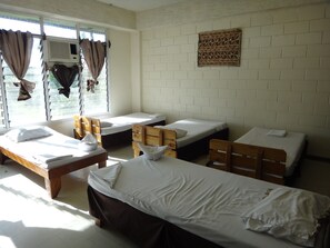 A dormitory room with four single beds, a wooden desk, and a window with curtains.