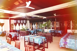 A restaurant with multiple tables and chairs, ceiling fans, and potted plants.