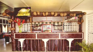 A bar area with a wooden backdrop, a television screen, and three white bar stools.