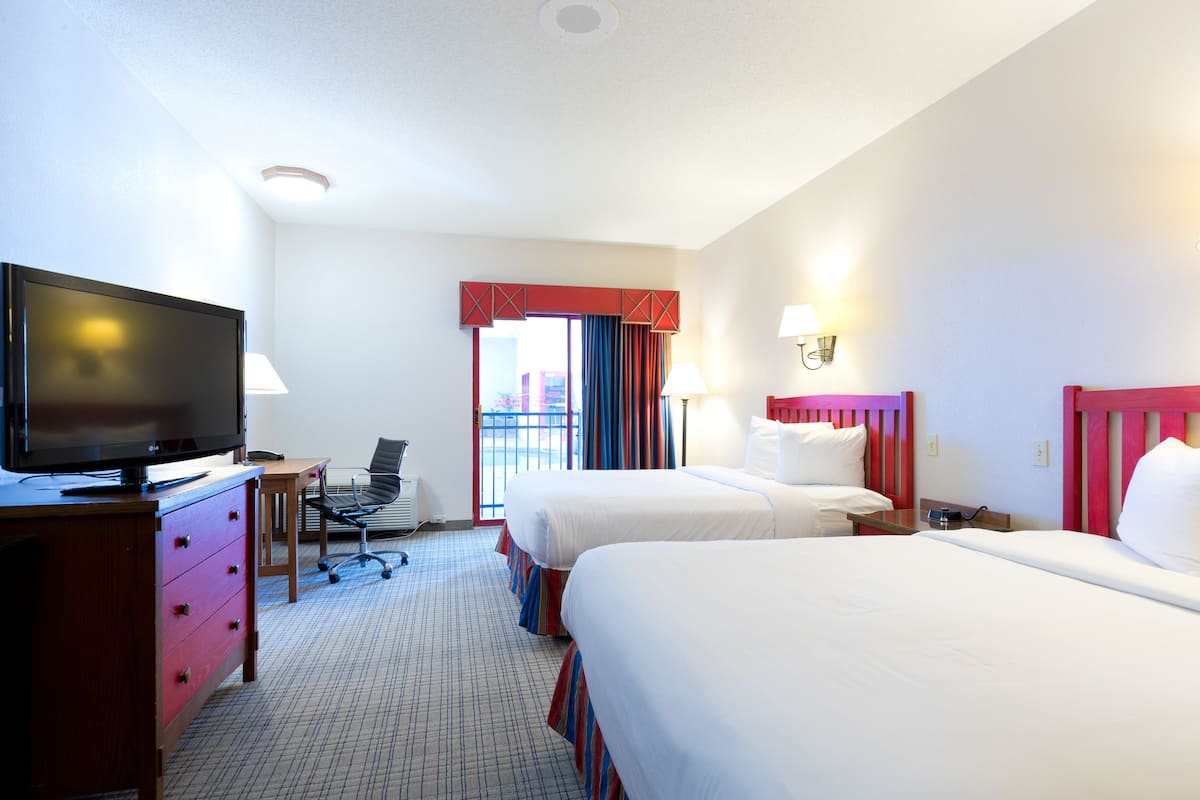 A hotel room with two beds, a desk with a television, a chair, and a window with curtains.