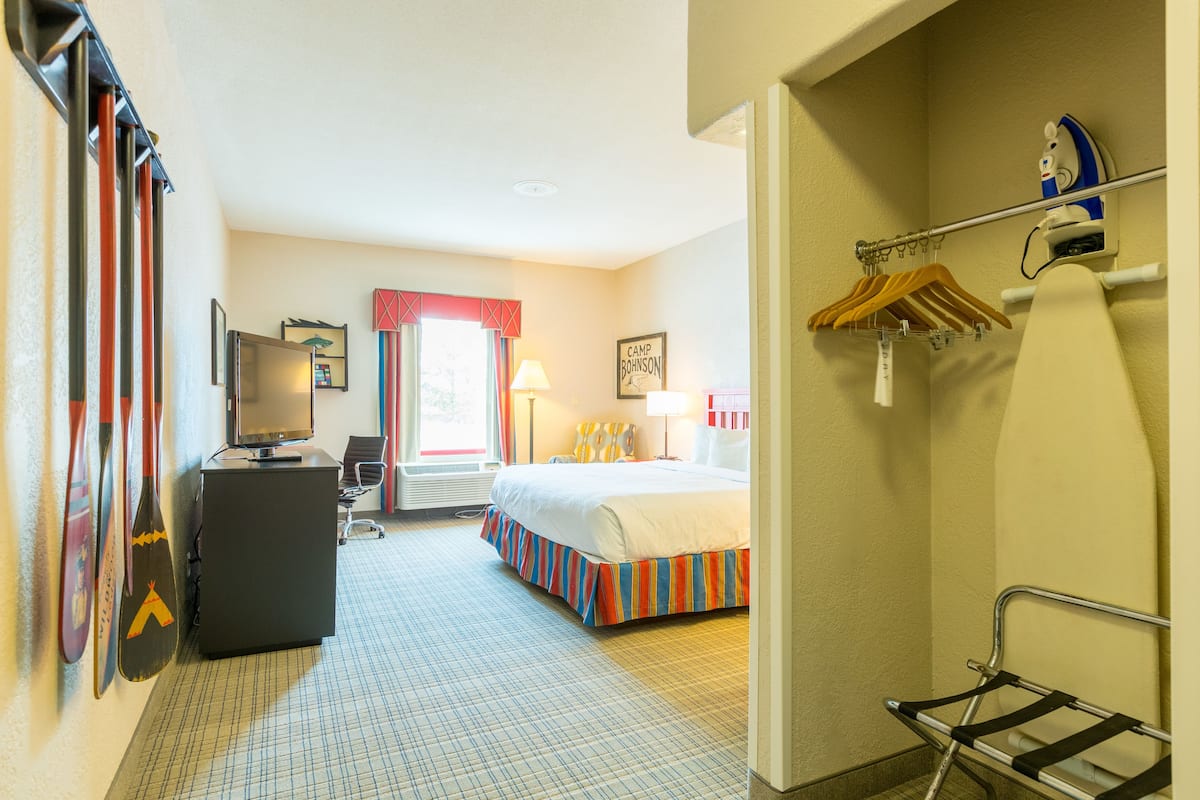 A hotel room with a bed, desk, television, and a coat rack.