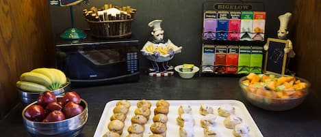 Un comptoir de cuisine sur lequel on trouve divers aliments, notamment un plateau de muffins, un bol de pommes, un bol de carottes et une sélection de boîtes de thé.