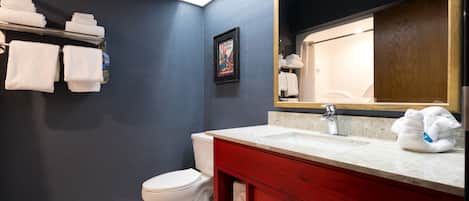 A bathroom with a white toilet, a red vanity with a mirror, and a towel rack with folded towels.