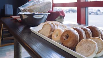 A tray of bagels and a bowl of soup on a wooden table in a room with a large window.