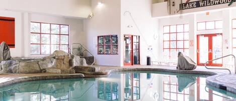 An indoor swimming pool with a rock feature, clear glass walls, and a sign reading "LAKE WILDWOOD".