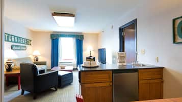 A compact hotel room with a kitchenette, a sofa, a small dining table, and a bed.