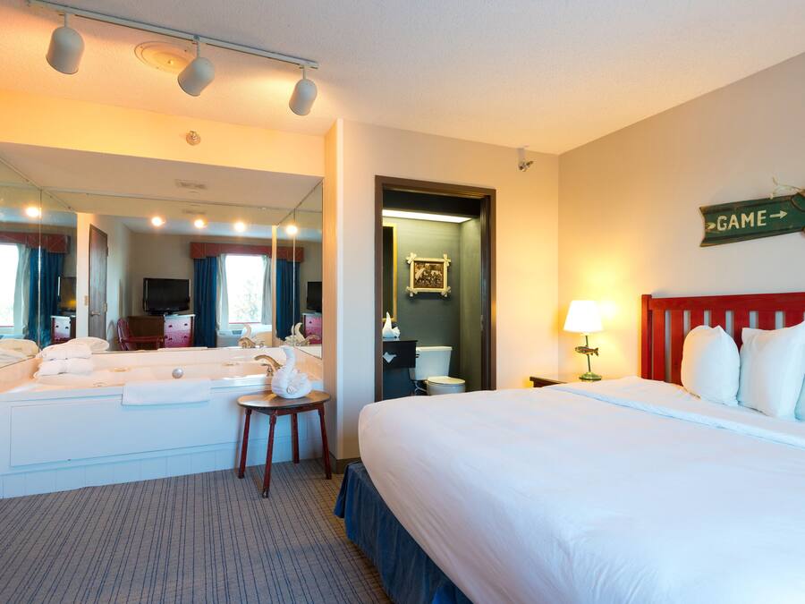 Una habitación de hotel con una cama grande, una zona de estar con una silla y una mesa, un baño con espejo y un letrero en la pared.