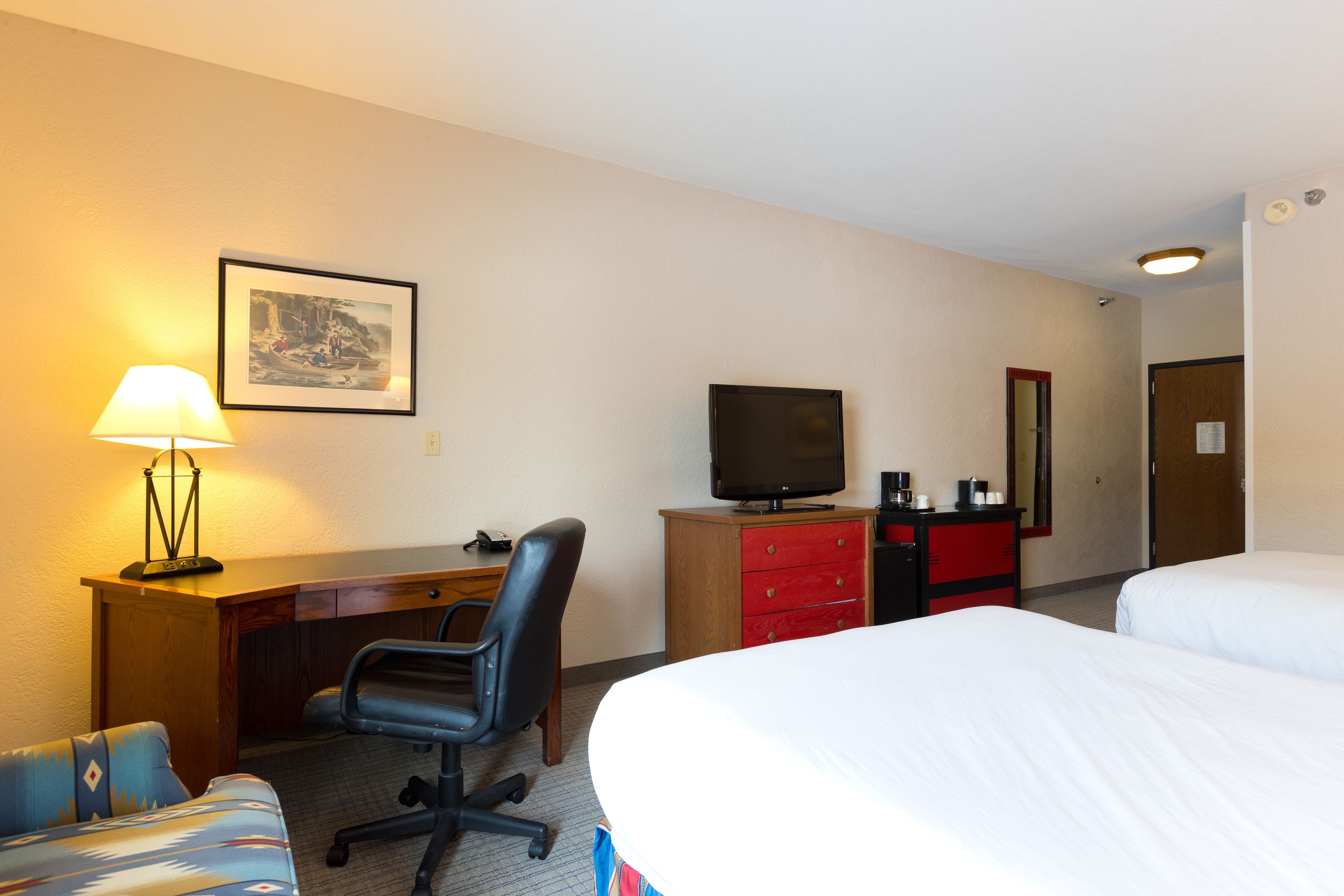A hotel room with a bed, a desk with a chair, a television, and a dresser.